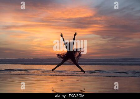 Junge Tänzerin chiffon Kleid, tanzen in der Luft, am Strand bei Sonnenuntergang, San Diego, Kalifornien, USA Stockfoto