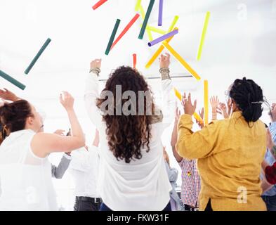 Hintere Ansicht Kolleginnen und Kollegen im Team-building-Aufgabe, die bunten Röhren in die Luft zu werfen Stockfoto