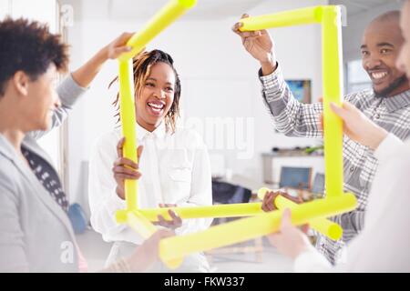 Kolleginnen und Kollegen im Team-building Aufgabe hält gelbe Rubes lächelnd Stockfoto