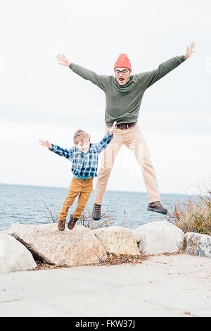 Vater und Sohn springen von Felsen am See Stockfoto