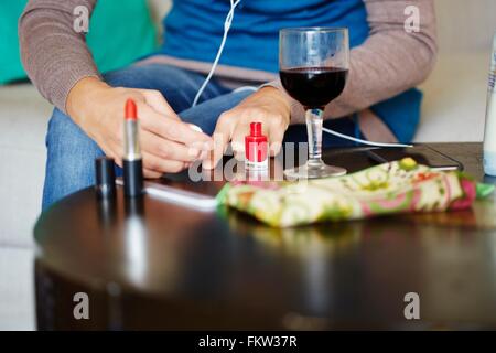 Junge Frau sitzt am Tisch, die Anwendung von Nagellack, Mittelteil Stockfoto