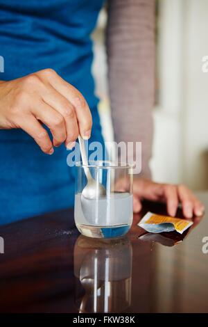 Junge Frau wasserlösliche Medikamente aus dem Beutel in Glas Wasser mischen Stockfoto