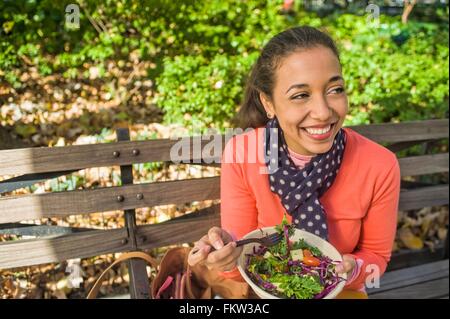 Junge Frau sitzt auf der Parkbank Essen Stockfoto