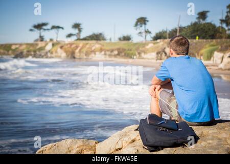 Junger Mann sitzen von Felsen, Blick auf das Meer, Rückansicht Stockfoto