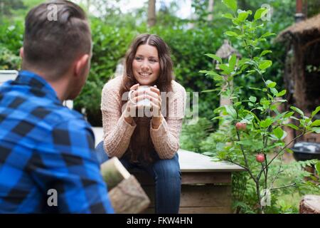 Junge Frau am Chalet Veranda Kaffee zu trinken, während Freund Protokolle trägt Stockfoto