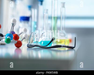 Schutzbrille und Molekülmodell am Labortisch, wissenschaftliche Ausrüstung im Hintergrund Stockfoto