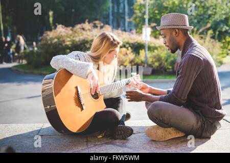 Paar im Park Gitarrespielen lernen Stockfoto
