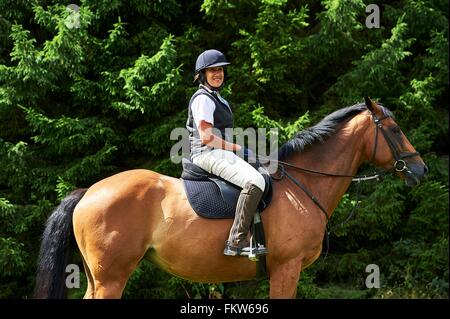 Seitenansicht des Reife Frau Reiten tragen Reiten Hut und Stiefel, Blick auf die Kamera zu Lächeln Stockfoto