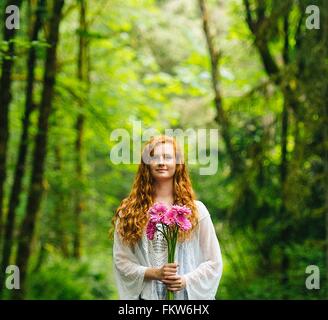 Junge Frau mit Haufen von rosa Gerbera im Wald Stockfoto