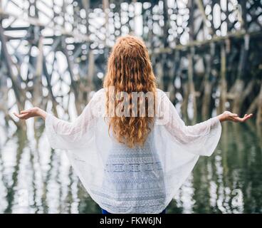 Rückansicht des Frau mit langen roten Haaren meditieren vor Holz River pier Stockfoto