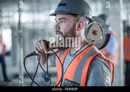 Junge männliche Baumeister tragen Runde sah auf Schulter auf Baustelle Stockfoto