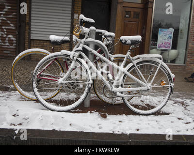 Geparkte Fahrräder auf dem Gehsteig entlang 7th Ave in Park Slope, Brooklyn, nach einer leichten Schnee. Stockfoto