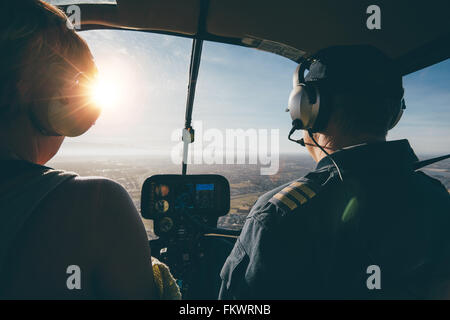 Zwei Piloten in einem Hubschrauber während des Fluges an einem sonnigen Tag. Rückansicht-Schuss von Mann und Frau Piloten Stockfoto