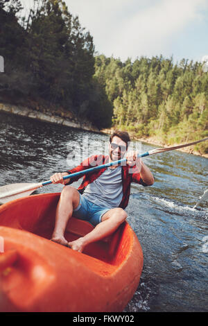 Porträt von lächelnden jungen Mann Kajak in einem See paddeln. Junger Kerl auf einem See paddeln. Stockfoto