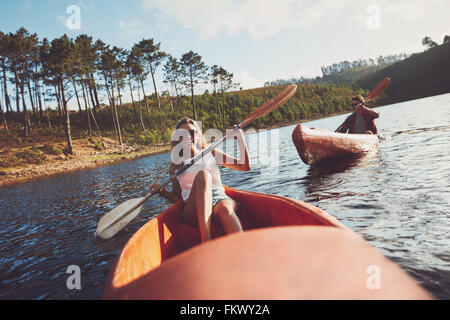 Junge Menschen an einem See paddeln. Lächelnde junge Frau Kajakfahrer mit einem Mann im Hintergrund Kajak zu paddeln. Stockfoto