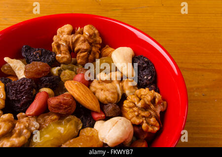 verschiedenen verschiedenen gemischten Nüssen und Rosinen in roten Platte auf hölzernen Hintergrund Stockfoto