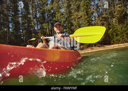 Senior kaukasischen Mann eine Kajak in See paddeln. Reifer Mann Kanu an Sommertag. Stockfoto