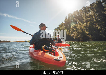 Im Freien Schuss von reifer Mann Kanu im See mit Frau im Hintergrund. Paar, Kajakfahren auf dem See an einem sonnigen Tag. Stockfoto