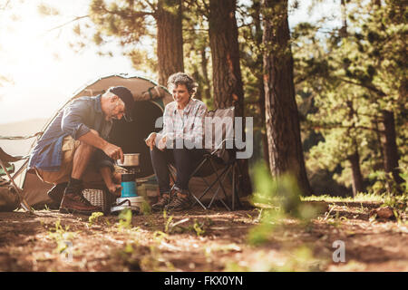 Happy Camper draußen in der Wildnis und Kaffeezubereitung auf dem Herd. Älteres Paar auf einem camping-Urlaub. Stockfoto