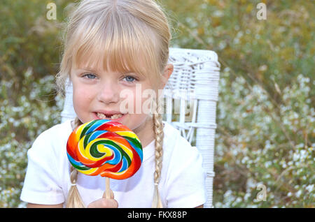 Blondes Mädchen mit fehlenden Frontzähne halten einen Regenbogen-Lutscher. Stockfoto