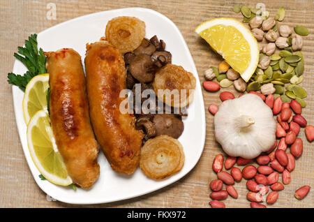 Gebratene Wurst mit Champignons und Zwiebeln auf einem weißen Teller. Stockfoto