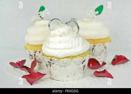 Trauringe in Cupcake Icing mit roten Rosenblättern. Stockfoto