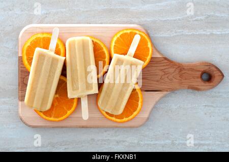 Gefrorenen orangener aromatisierter Joghurt knallt mit FRUCHTSCHEIBEN auf einem hölzernen Paddel-board Stockfoto