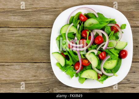 Salat mit Gemüse, Cherry-Tomaten, rote Zwiebeln und Gurken auf weißen Teller mit Holz Hintergrund, Draufsicht Stockfoto