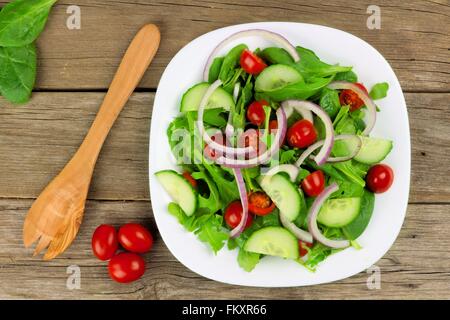 Salat mit Gemüse, Cherry-Tomaten, rote Zwiebeln und Gurken auf weißen Teller mit Holz Hintergrund, Draufsicht mit Gabel Stockfoto