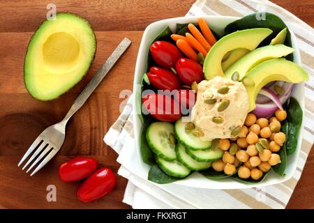 Gesundes Mittagessen Schüssel mit Avocado, Hummus und frisches Gemüse, obenliegende Szene auf Holztisch Stockfoto