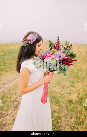 Brünette Braut mit Blumenstrauß in der Hand auf dem Feld. Nebel-Hintergrund Stockfoto
