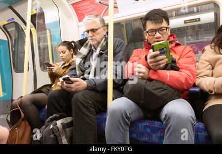 Mobiltelefone im öffentlichen Verkehr; Passagiere, die Mobiltelefone in einer Eisenbahn-Kutsche der Londoner U-Bahn, London UK, verwenden Stockfoto