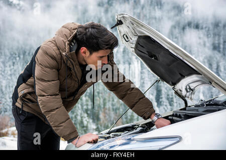 Junger Mann in der Nähe von Auto mit offener Haube Motor Inspektion. Verschneiten Wald auf Hintergrund Stockfoto