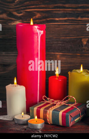 Kleine Geschenk-Boxen und Kerzen vor einer Holzwand Stockfoto