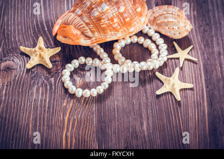 Meer Objekte - Muscheln, Seesterne, Perlen auf dunklem Holz. Stockfoto