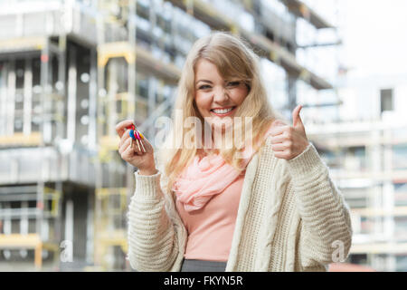 Immobilien-Konzept - junge Frau auf der Vorderseite des neuen großen modernen Hausbau Baustelle mit Tasten machen Daumen Zeichen Geste Stockfoto