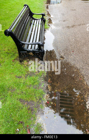 Blockiert ablassen und eine Pfütze von Regenwasser neben einer Bank in einem Park, Nottinghamshire, England, Großbritannien Stockfoto