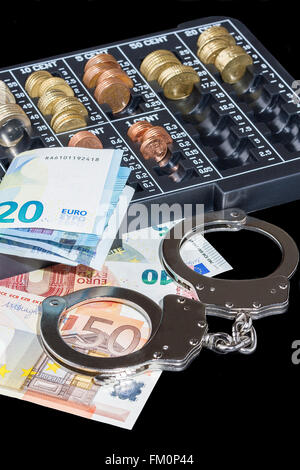 Handschellen, Euro-Scheine und Organisator der Euro-Münzen auf schwarzem Hintergrund Stockfoto
