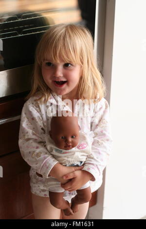 Glückliche kleine blonde Mädchen Kind stehend spielen Black baby doll sorglos und glücklich, Kinderspielzeug, Kindheit Kreativität, Spaß, Freude, Kindheit Konzept Stockfoto