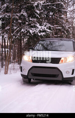 Modernes Auto mit leuchtenden Scheinwerfern auf Winter-Straße in Wald Stockfoto