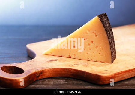 Stück Gruyere Käse auf Holzbrett schönen dunklen Hintergrund Stockfoto