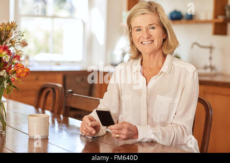 Ältere Frau lächelnd halten Sie eine Telefon in ihrer Küche Stockfoto