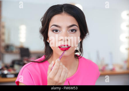 Zarte attraktive junge Frau, die roten Lippenstift mit Pinsel Stockfoto