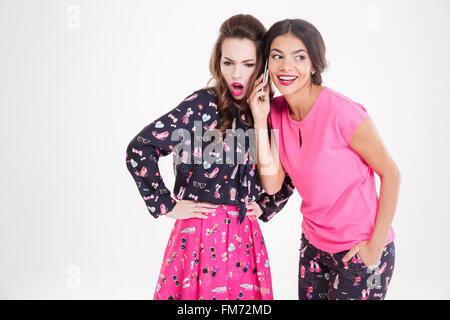 Zwei hübsche junge Frauen hören Gespräch am Handy auf weißem Hintergrund Stockfoto