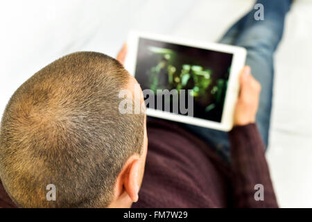 ein junger kaukasischer Mann auf der Couch liegen Uhren einen Film oder eine Serie in streaming auf seinem Tablettcomputer Stockfoto