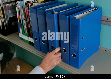 Hand, die blauen Hebel Bogen Datei Regal mit anderen Hebel-Bogen-Dateien Stockfoto