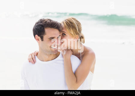 Junge Frau Flüstern mans Ohren am Strand Stockfoto