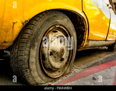 Reifenpanne von einem alten gelben Auto mit verrosteten Felge. Stockfoto