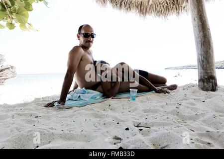 Cuba, Holguin, Guardalavaca, paar liegen auf dem weißen Sand im Schatten der Palmen Sonnenschirm Stockfoto