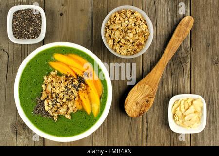 Grüner Smoothie Schüssel mit Mangos, Müsli, Mandeln und Chia Samen, obenliegende Szene auf Holz Stockfoto